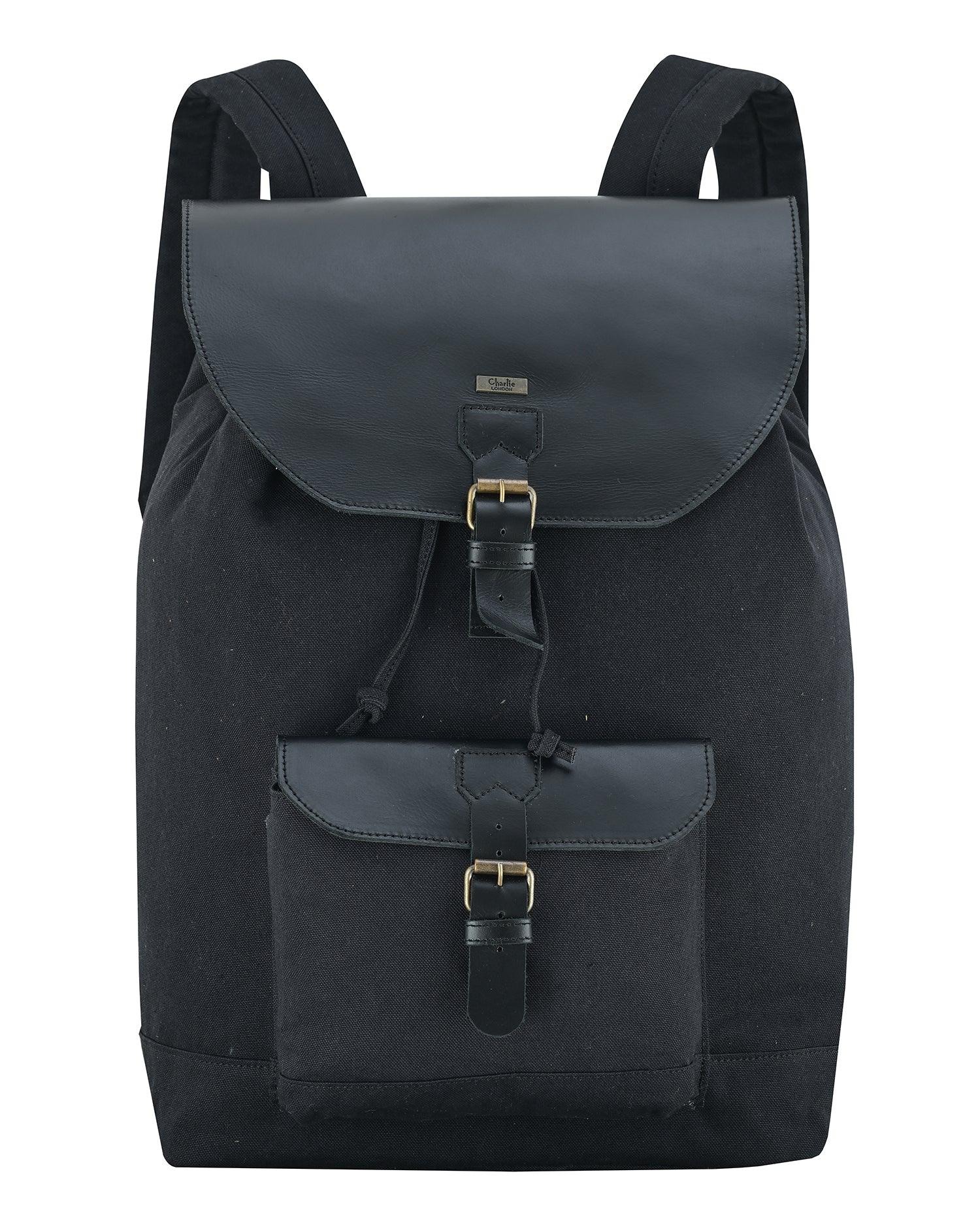 A black canvas backpack with dark gray leather-like trim and gold-tone buckle details, shown against a plain white background.